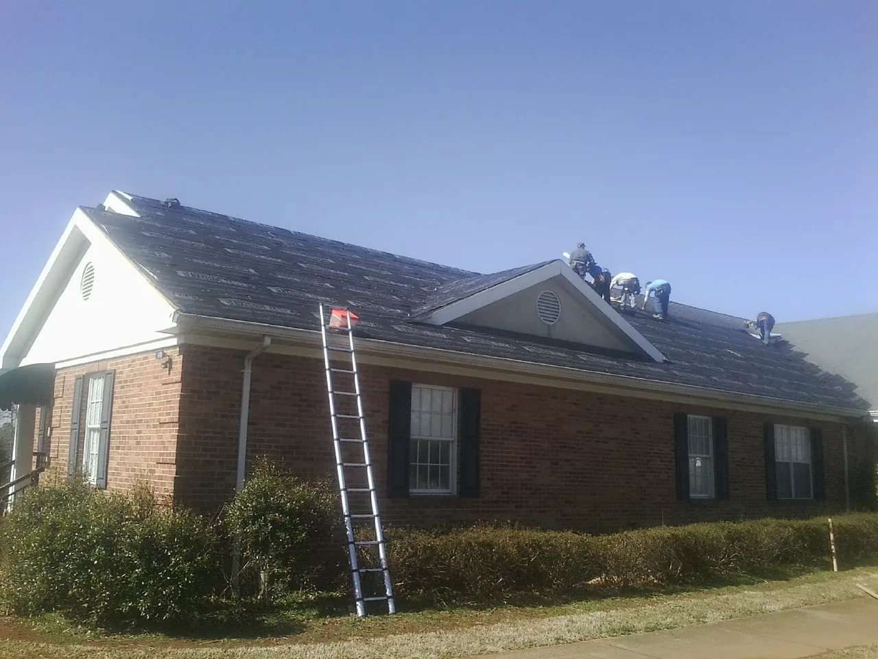 Crew tearing shingles off a brick ranch roof with a ladder set — Emergency Roof Repair work by our crew in Casselberry