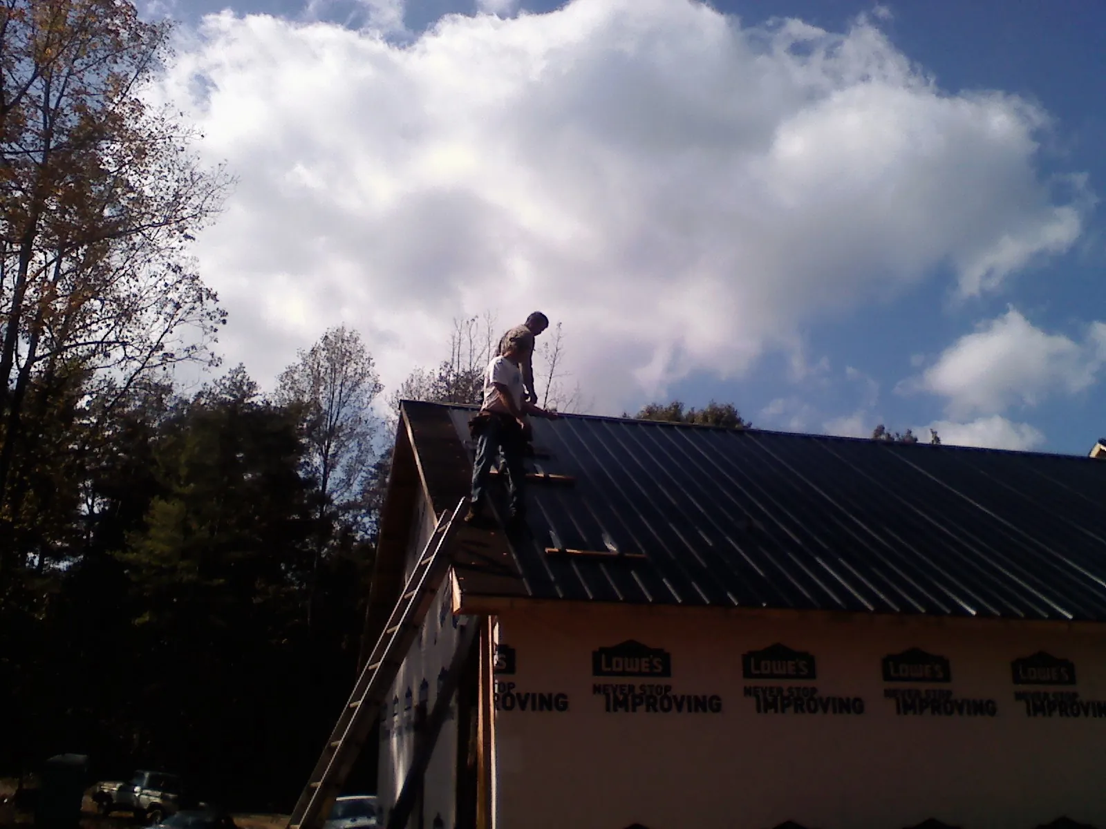 Roofer fastening dark metal panels high against a cloudy sky, from a Roof Inspection job in Casselberry
